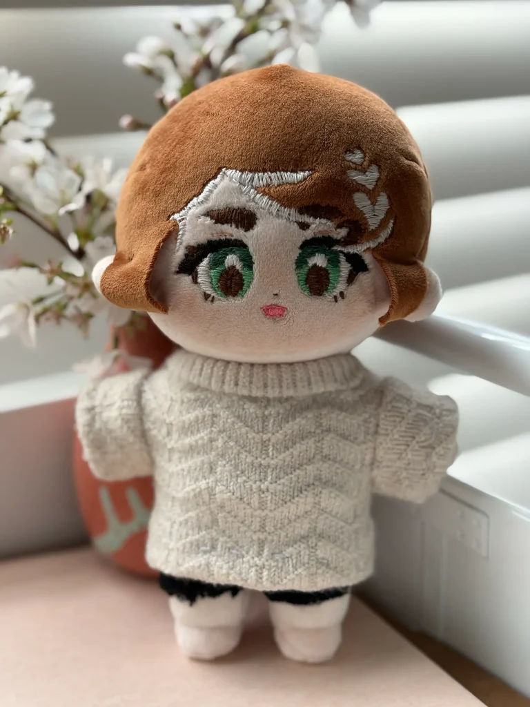 Close-up of a doll's embroidered face with green eyes, brown lashes, and a white heart design in the hair.